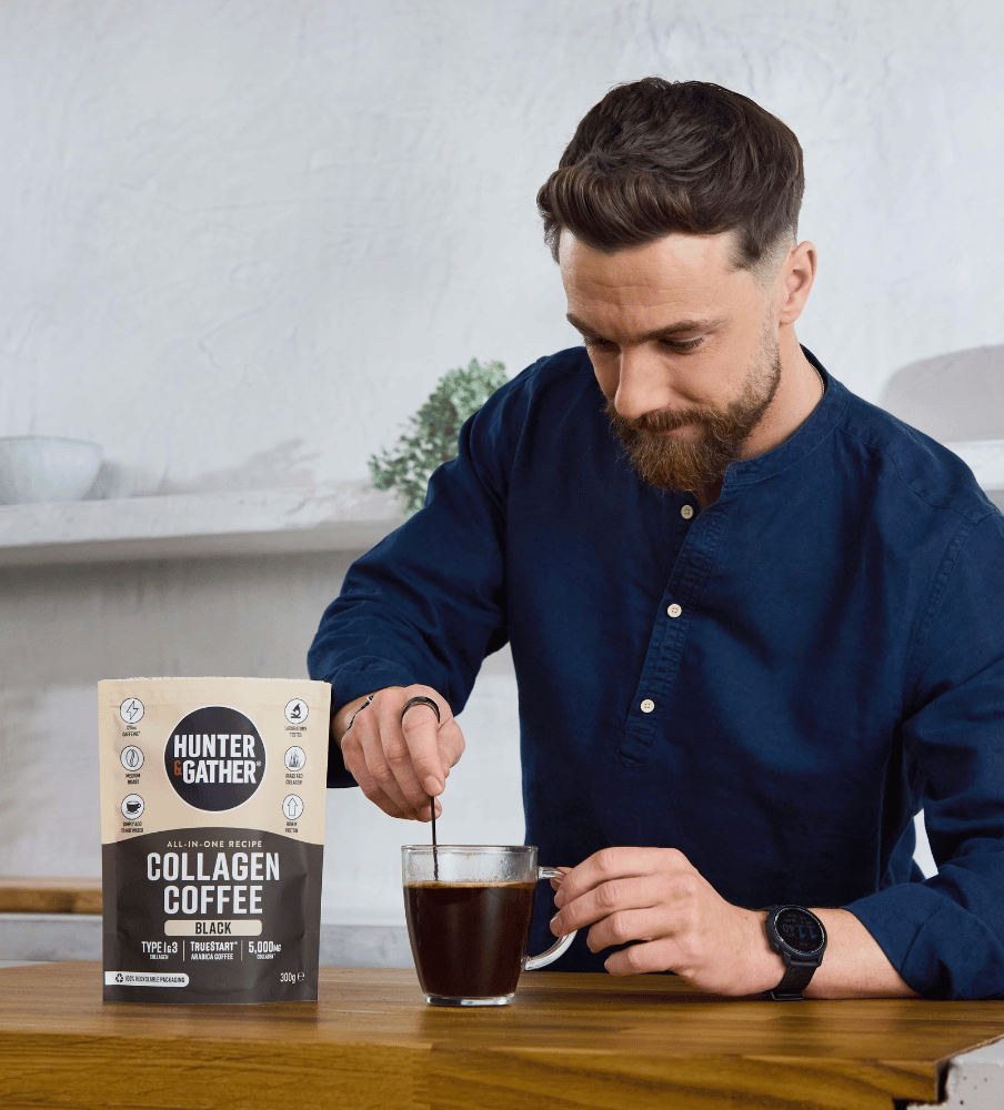 Man stirring a cup of coffee with a Hunter Gather collagen coffee package on a table.