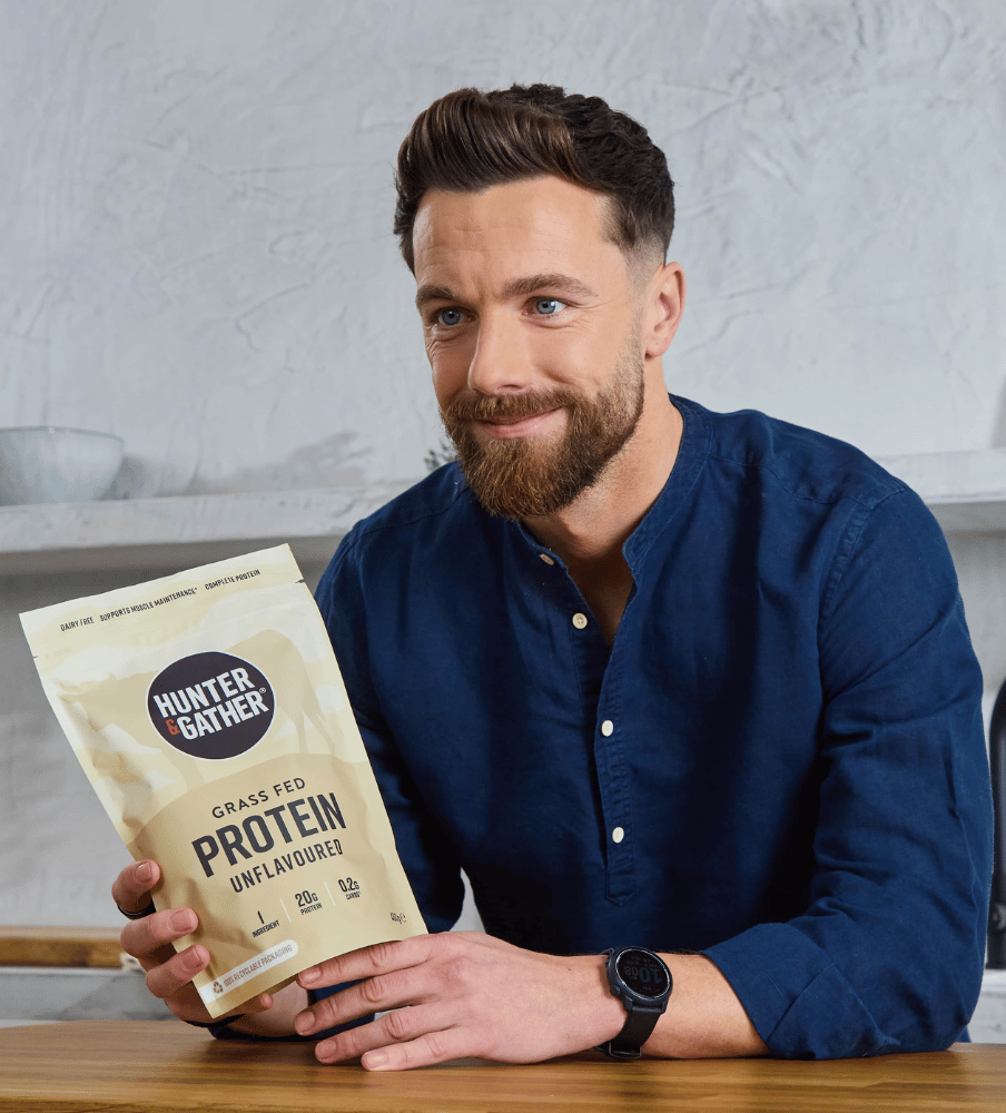 Man holding a Hunter & Gather protein powder package in a kitchen setting